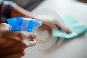 Cleaning home surface with sponge and spray cleaner. Female hands using spray cleaner on white table. Maid wiping dust while