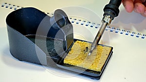 Cleaning the hot tip of his soldering iron on a wet sponge pad.