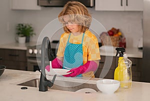 Cleaning house. Child boy washing the dishes in the kitchen sink. Detergents and cleaning accessories. Cleaning service