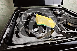Cleaning the kitchen, cleaning the surface on a black gas stove with a washcloth and foam