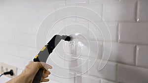 Cleaning kitchen tiles with steam. A woman washes ceramic tiles in a bathroom with a steam generator. Steam cleaning