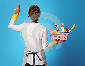 Cleaning lady with a basket with cleansers and brushes pointing