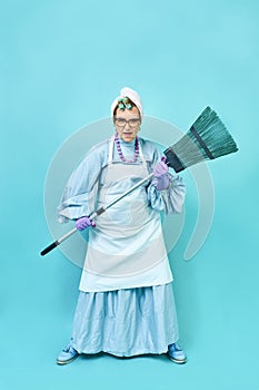 Cleaning Lady Fun. Elderly funny housewife fooling around with a broom. Full body isolated blue