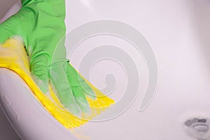 Cleaning lady in green gloves cleans the sink in the bathroom