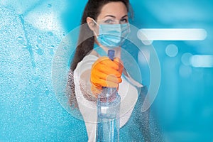 Cleaning lady in a mask disinfects a blue background
