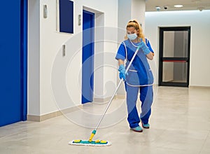 A cleaning lady with a mask on her face cleans the hallway photo