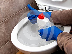 The cleaning lady near the toilet with cleaning agent shows the ok sign with her hand. The toilet is clean