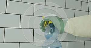 Cleaning lady sprays a cleaning agent on the white tiles on the wall. Apartment cleaning, cleaning services.