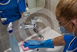 A cleaning leady with mask on her face cleans the washbasin