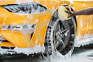 Cleaning of modern rims of luxury yellow car at self car wash service outdoors.