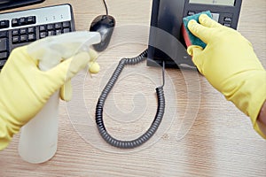 Cleaning the office, a janitor in yellow gloves wipes telephone and computer equipment with a rag