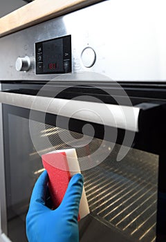 Cleaning the oven outside. A female hand in household cleaning gloves cleans the glass and oven panel.Close up of female hands wit