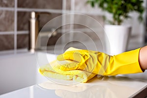 Cleaning and polishing bathroom. Female hand in yellow gloves on white surface of sink. Housekeeping and hygiene
