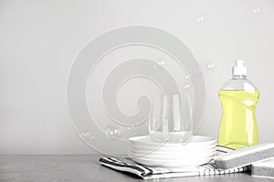 Cleaning product, plates and soap bubbles on grey background, space for text. Dish washing supplies