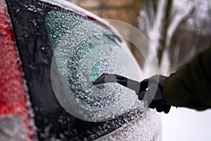 Cleaning the rear car window of snow with ice scraper before the trip. Man removes ice from car rear window wiper. Male