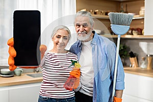 Cleaning Service App. Senior Couple Showing Blank Smartphone While Standing In Kitchen