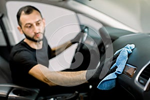 Cleaning service, car detailing concept. Young man, auto service worker, washing a car interior, console and dashboard