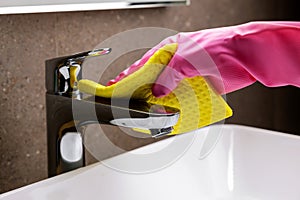 cleaning service and chores. hand with rubber glove and sponge cleans the bathroom sink chrome faucet