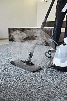 Cleaning service company employee removing dirt from carpet in flat with professional steam cleaner equipment close up