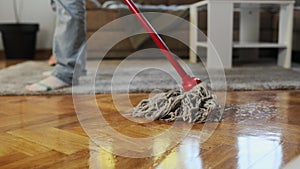 Cleaning service. Housewife mopping parquet with wet mop. Close-up of washing floor. Follow shot. Low angle view
