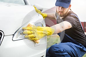 Cleaning service. Man in uniform and yellow gloves washes a car body in a car wash