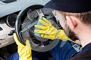 Cleaning service. Man in uniform and yellow gloves washes a car interior in a car wash