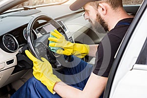 Cleaning service. Man in uniform and yellow gloves washes a car interior in a car wash