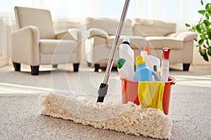 Cleaning set for different surfaces in orange bucket and mop on floor in living room, copy space. Cleaning service concept.