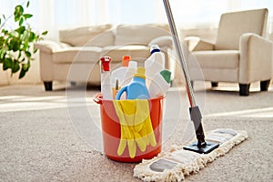 Cleaning set for different surfaces in orange bucket and mop on floor in living room, copy space. Cleaning service concept.