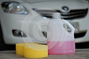 Cleaning shampoo and sponge on car background