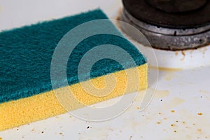 A cleaning sponge lies on a dirty kitchen stove
