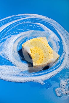 cleaning sponge wiping foam soap suds on blue background, household washing concept