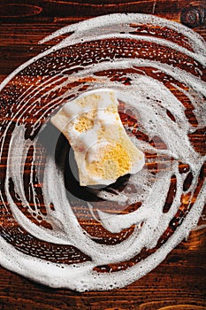 cleaning sponge wiping foam soap suds on wooden background, household washing concept