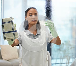Cleaning spray, woman and home with cloth and living room task with washing glass. Young female person, maid and apron