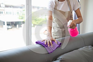 Cleaning staff is wiping cloth with cleaner and disinfectant on the surface of sofa to make the sofa clean with cleaning products