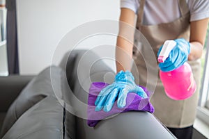 Cleaning staff is wiping cloth with cleaner and disinfectant on the surface of sofa to make the sofa clean with cleaning products