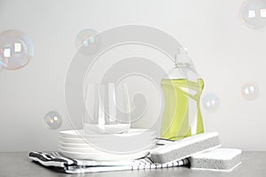 Cleaning supplies for dish washing, plates and soap bubbles on grey background