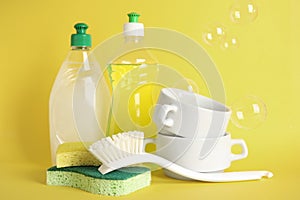 Cleaning supplies for dish washing and soap bubbles on yellow background