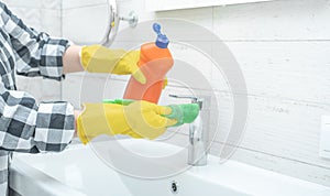 Cleaning Tap. Man doing chores cleaning bathroom at home. Cropped view of woman in rubber gloves with wet rag and detergent
