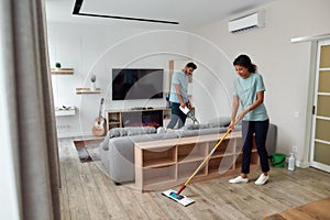 Cleaning team. Two professional cleaners in uniform working together in the living room. Young afro american woman