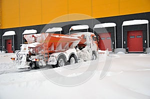 Cleaning the territory of a modern warehouse complex from snow accumulations with specialized road equipment.