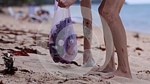 Cleaning tropical beach from plastic trash. Male volunteer collects up garbage in trash purple bag. Environmental