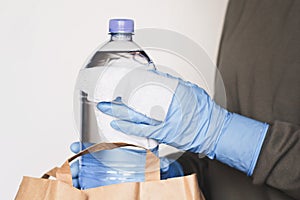 Cleaning water bottle surface with disinfecting wipe. Woman wearing protective blue rubber gloves cleaning packages