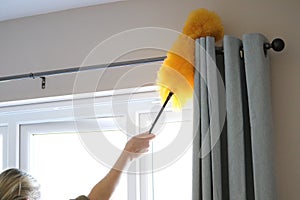 Cleaning the window and curtains area with a fluffy yellow duster