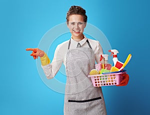 Cleaning woman with basket with cleansers and brushes pointing