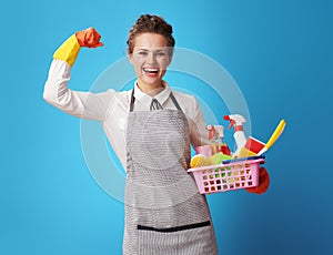 Cleaning woman with a basket with cleansers and brushes showing