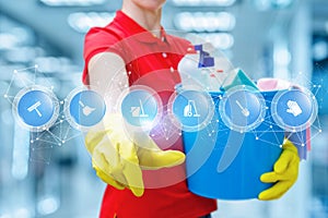 A cleaning woman in rubber gloves is keeping a bucket fulfilled with chemicals and touching a screen with digital scheme of many photo