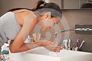 Cleanliness is next to godliness. A beautiful young woman washing her face in her bathroom. photo