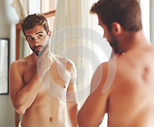 Cleanliness is next to godliness. a shirtless young man checking out his skin in the bathroom mirror. photo