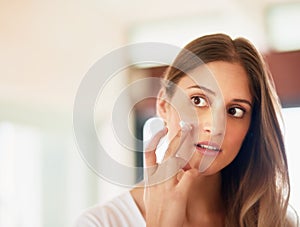 Cleanse, tone, and moisturise to protect your healthy skin. a young woman applying moisturiser to her face.
